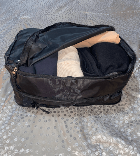 well traveled packing cube black cube open zipper rolled clothing inside on gray bedspread