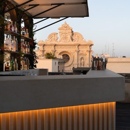 Patria Palace Lecce Hotel rooftop bar white countertop evening sky alcohol bottles on bar shelves