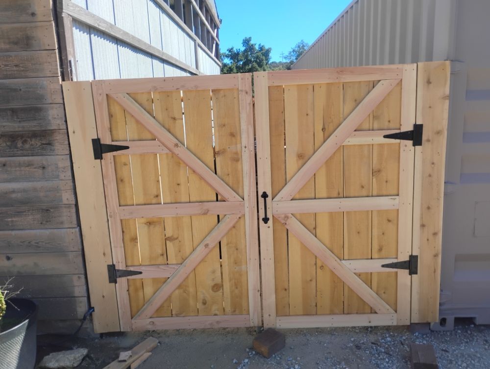 A wooden gate with black hinges is sitting in front of a building.