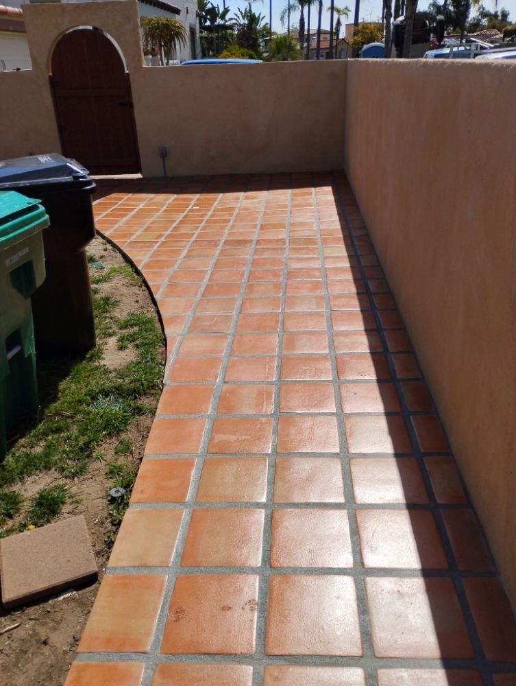 A tiled walkway leading to a trash can and a wall.