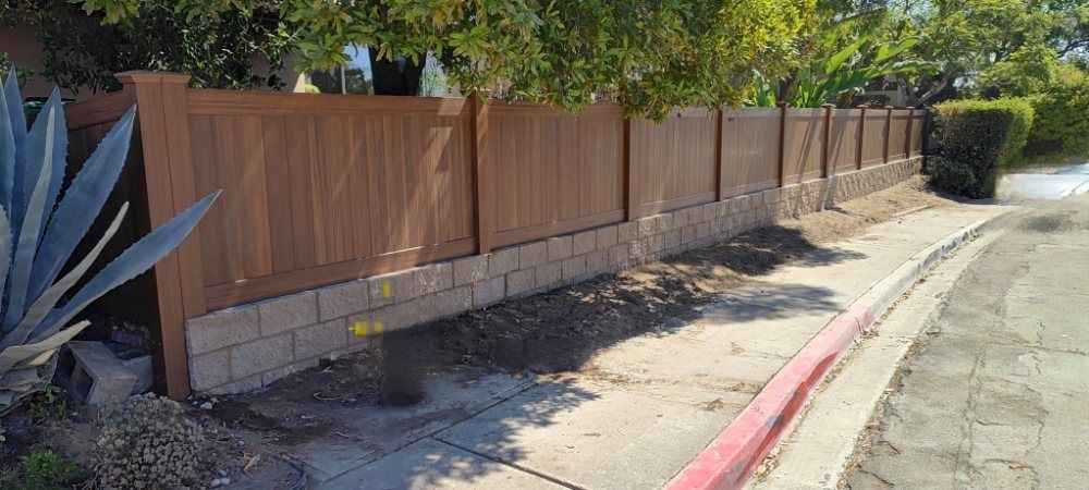 A wooden fence is sitting next to a brick wall on the side of a road.