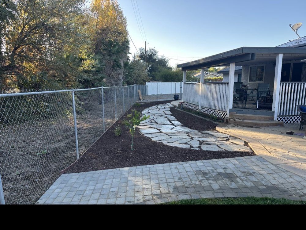 A brick walkway leading to a house with a chain link fence.