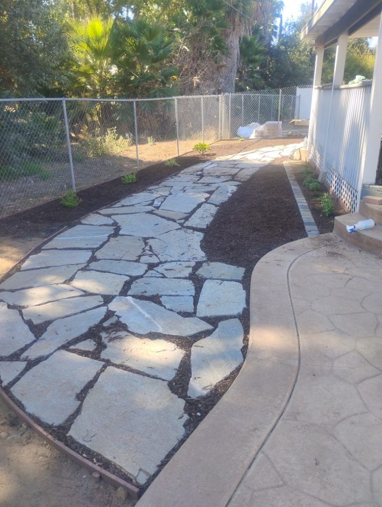 A stone walkway leading to a house with a fence in the background.