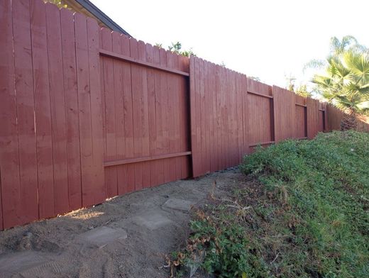 A red wooden fence is surrounded by grass and dirt.