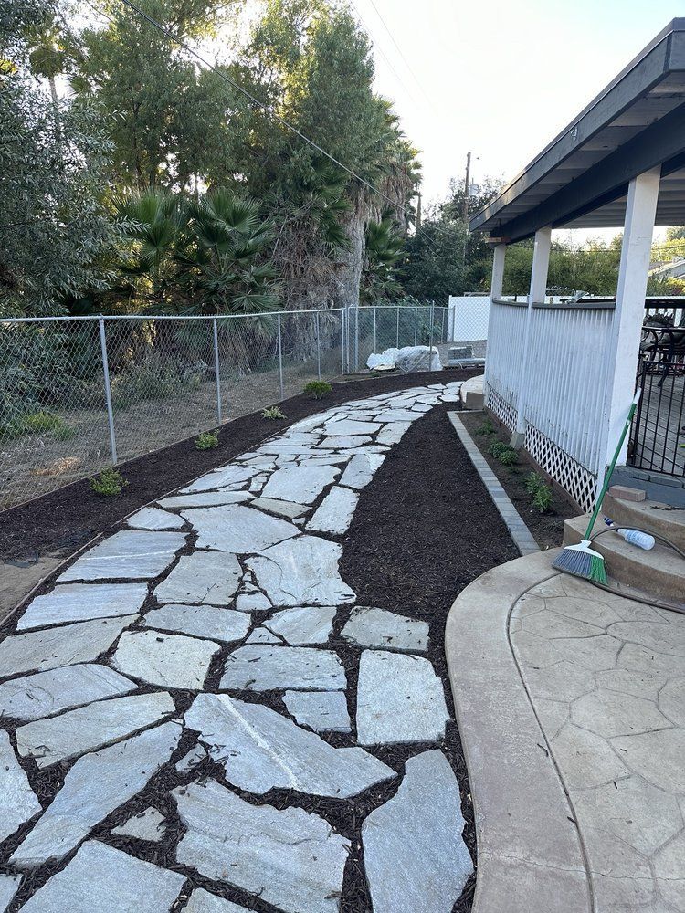 A stone walkway leading to a house with a fence in the background.