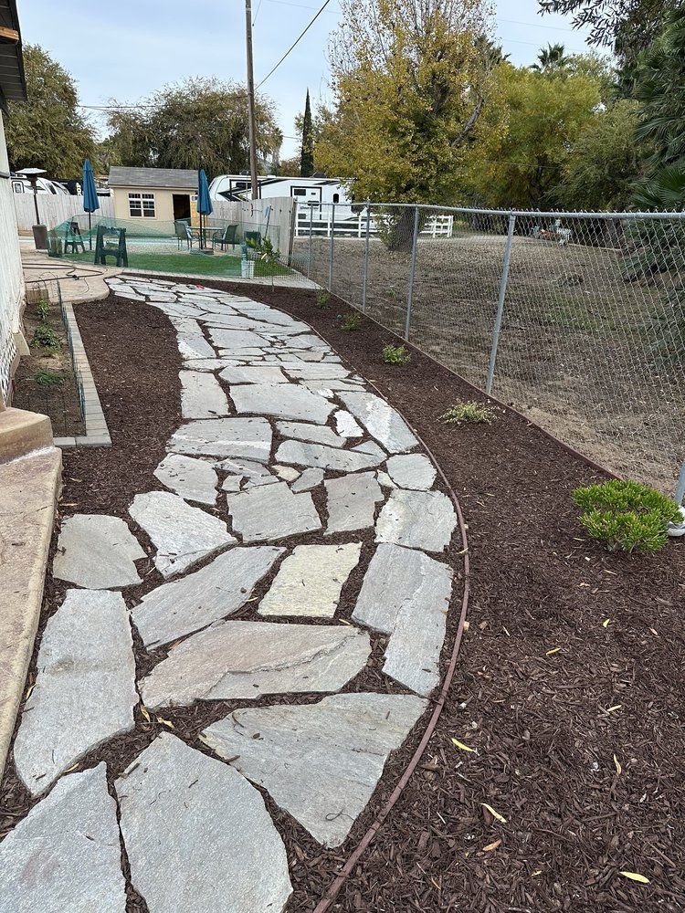 A stone walkway leading to a house with a fence in the background.