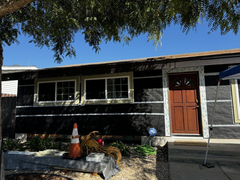 A house is being remodeled with black siding and a red door.
