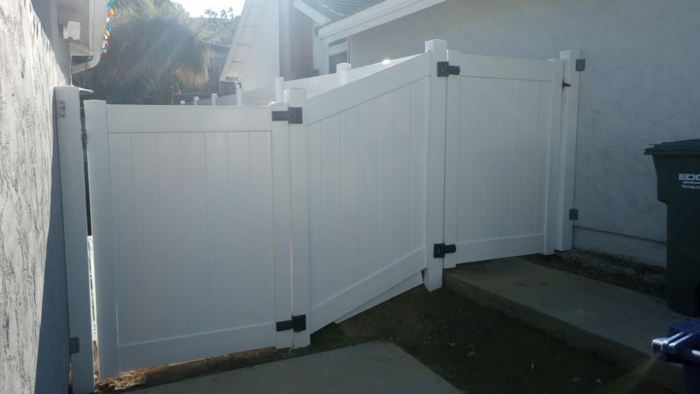 A white vinyl fence is sitting next to a trash can.