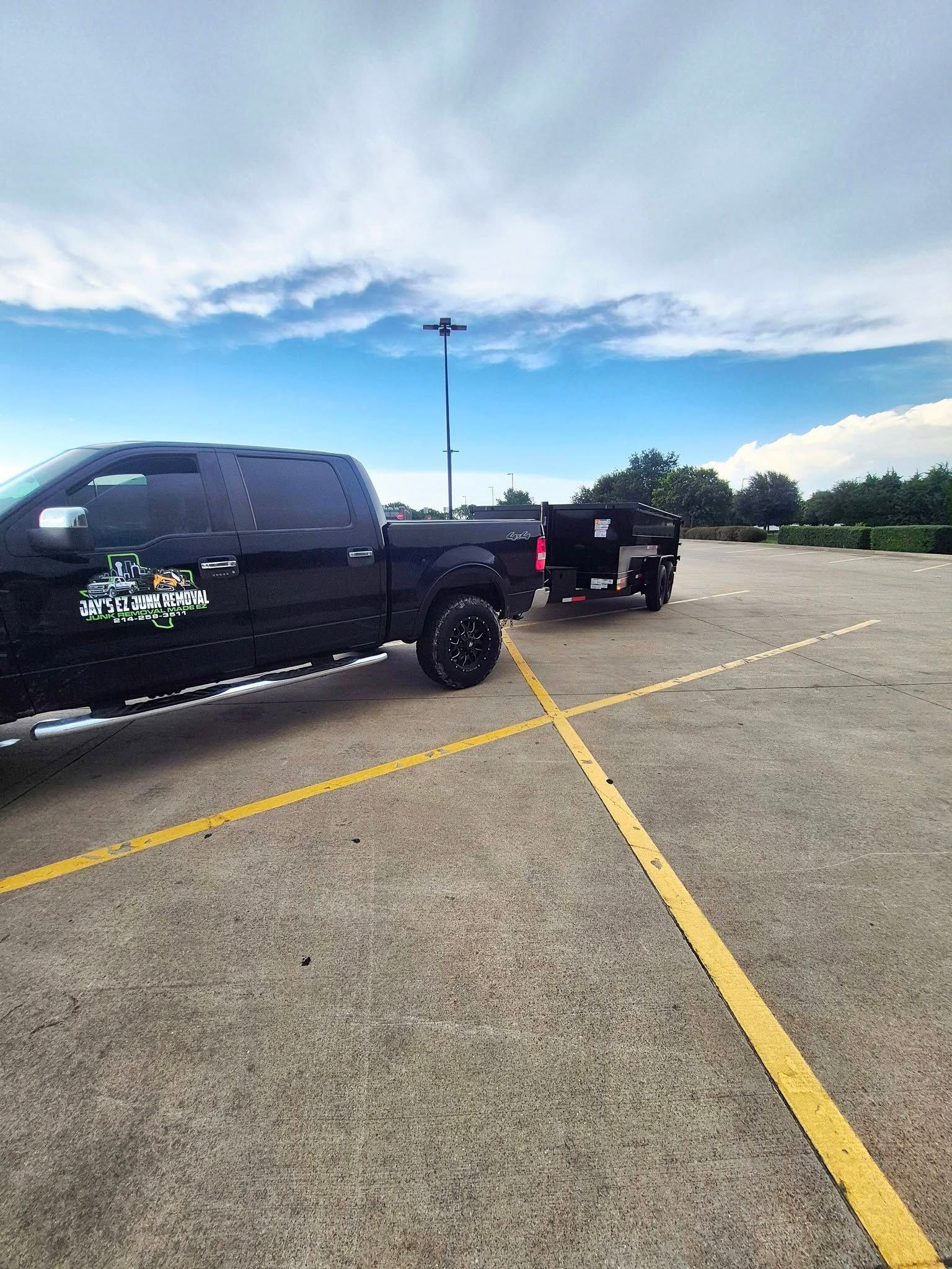 Black truck towing a black trailer in an empty parking lot under a cloudy sky.