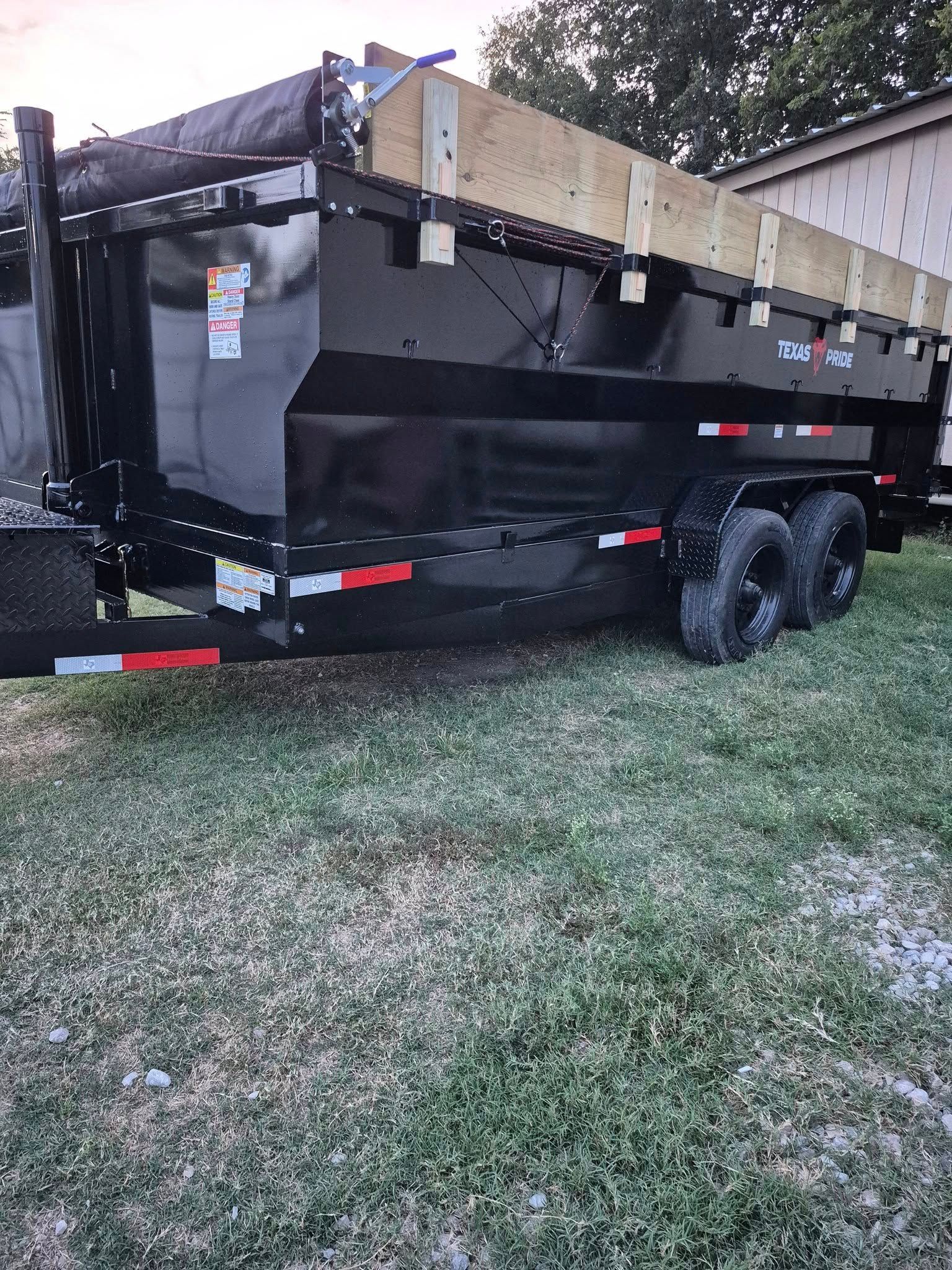 Black dump trailer on grass, with wooden extensions on sides.