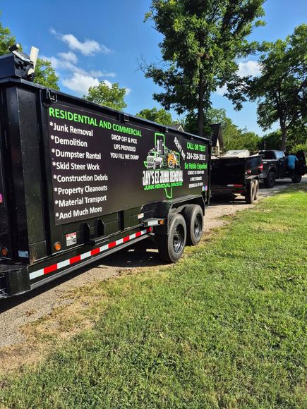 Black dumpster trailer with residential and commercial removal services listed, parked on grass.