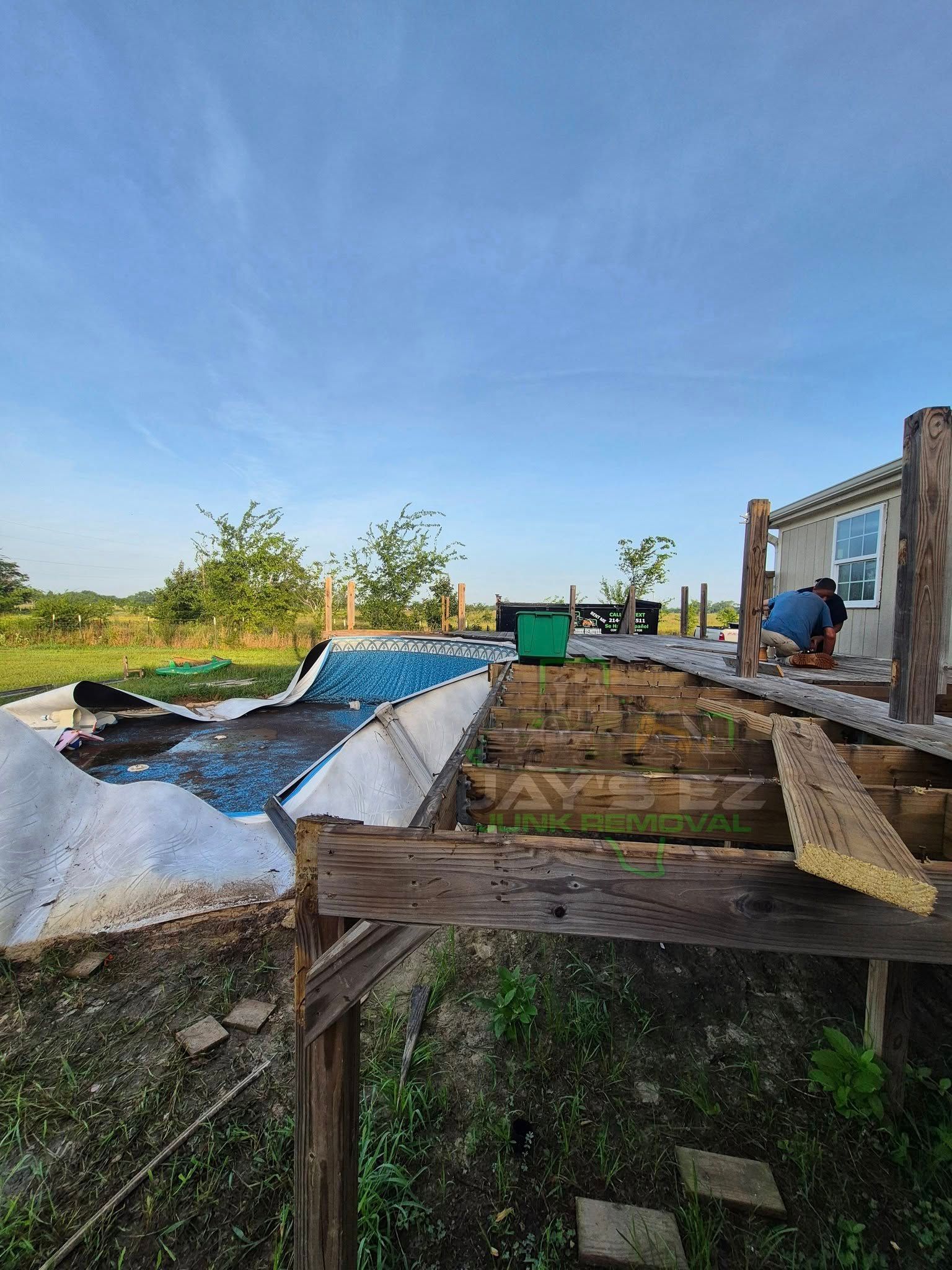 Man repairing a weathered wooden deck outdoors under a blue sky.
