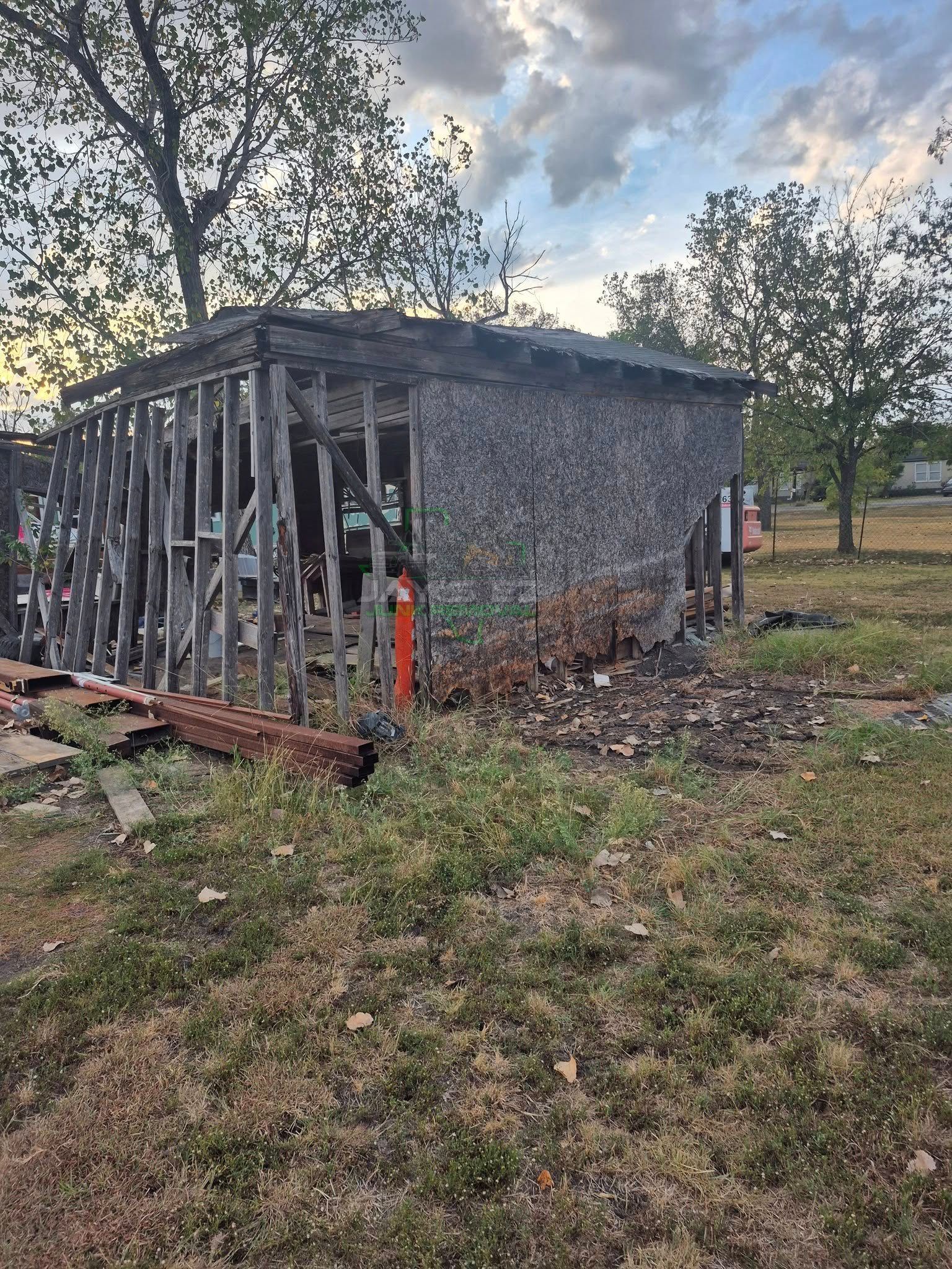 Dilapidated wooden shed with missing siding, weathered exterior, and overgrown grass.
