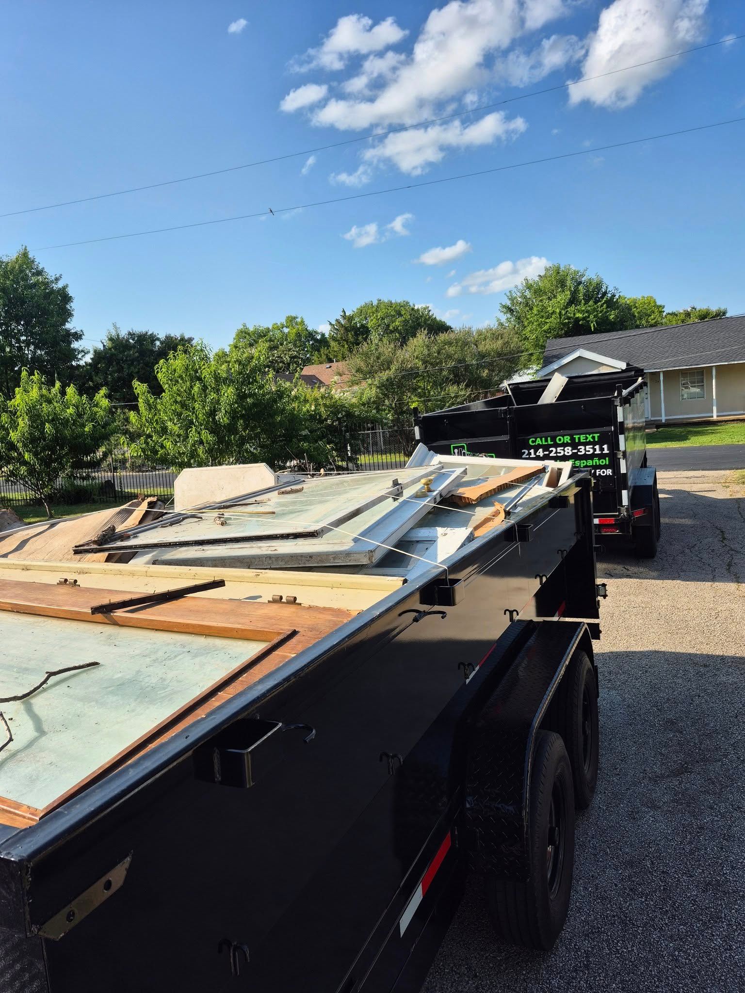 A black trailer loaded with construction debris parked outside a house under a cloudy sky.
