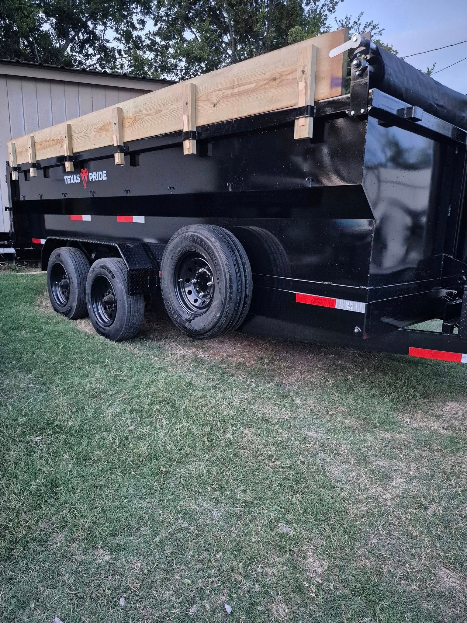 Black dump trailer with wooden side extensions, parked on grass.