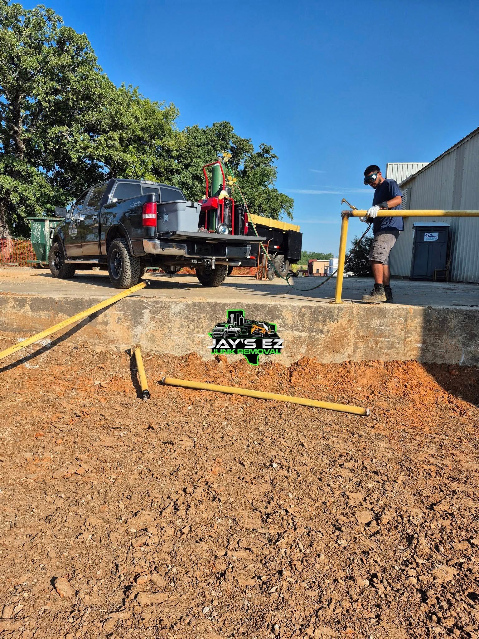 Truck with equipment, a person working near a yellow railing, and a ground area with a machine. Sunny day.