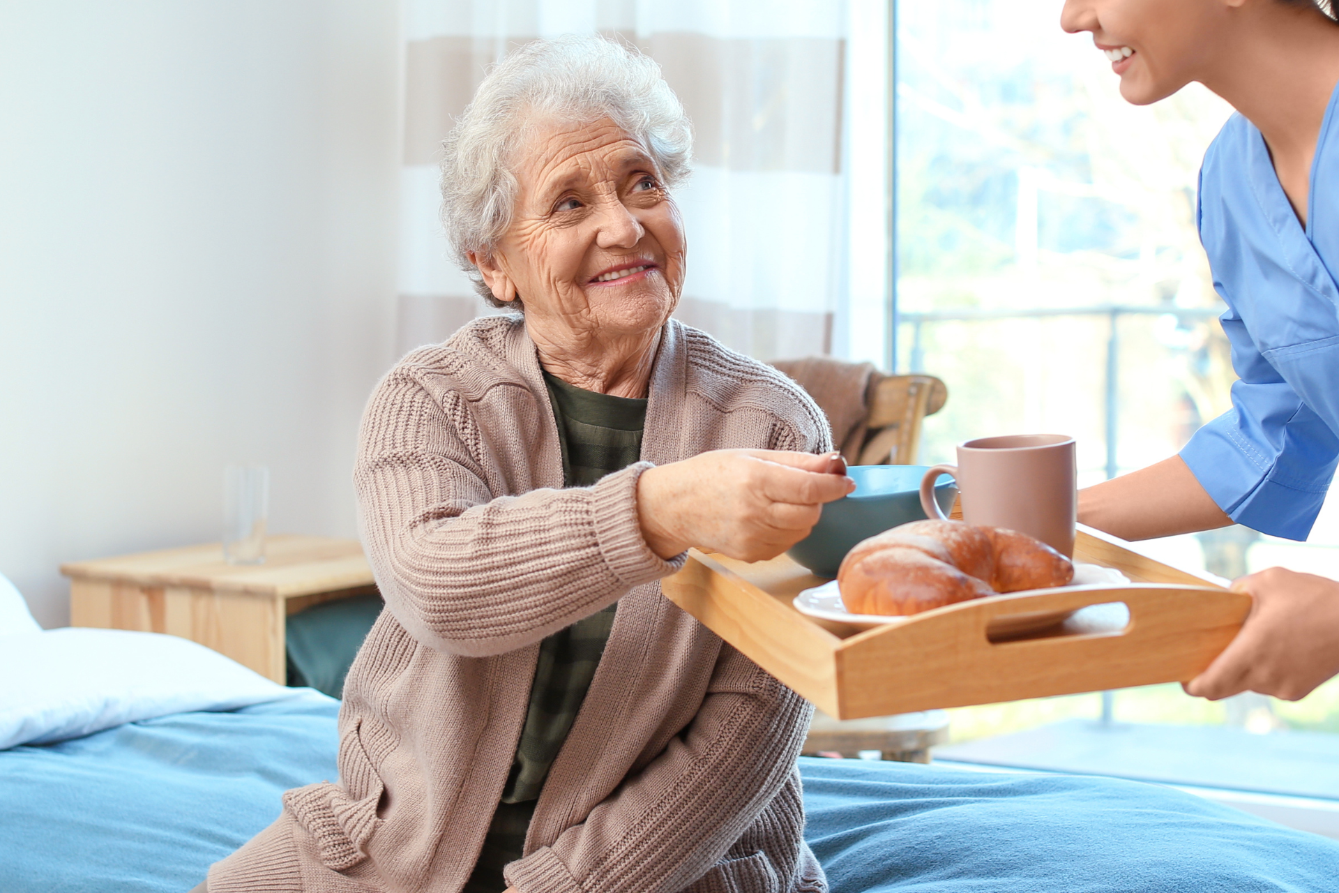 Smiling senior woman in glasses, seated at a table, speaking to a person with their back to the camera.