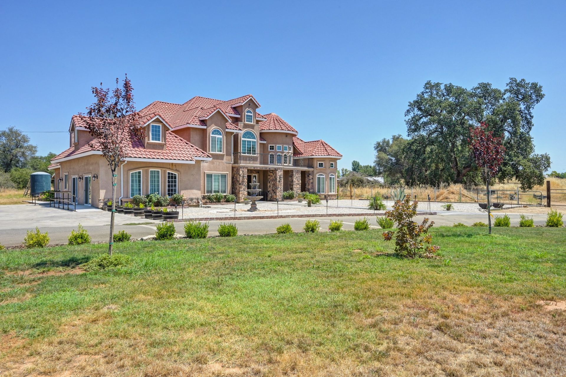 Large stucco home with red tile roof on a grassy lot, clear blue sky.