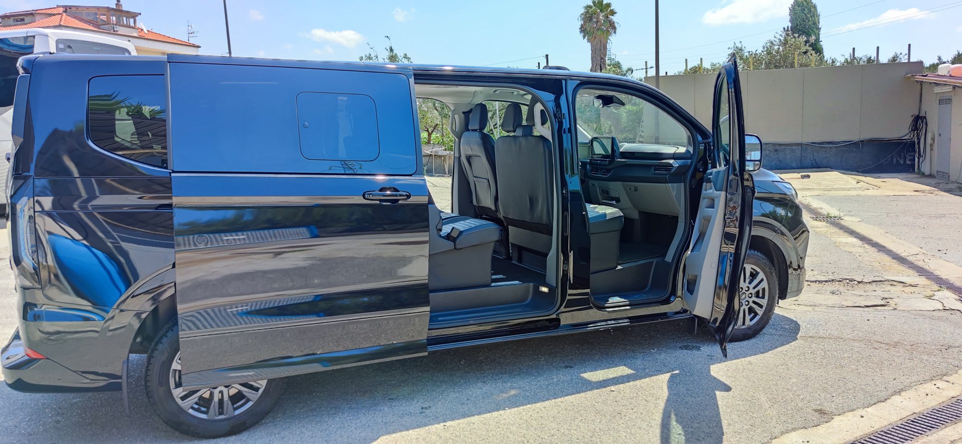 Furgone nero con portiere aperte parcheggiato all'aperto in una giornata di sole. I sedili interni sono visibili; 