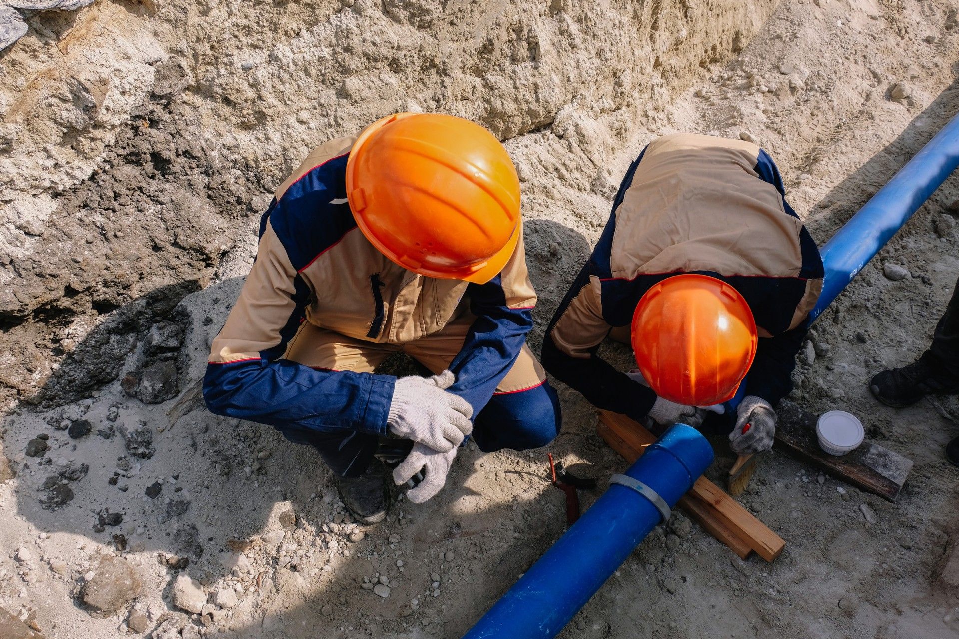 Two construction workers are working on a pipe in the dirt.