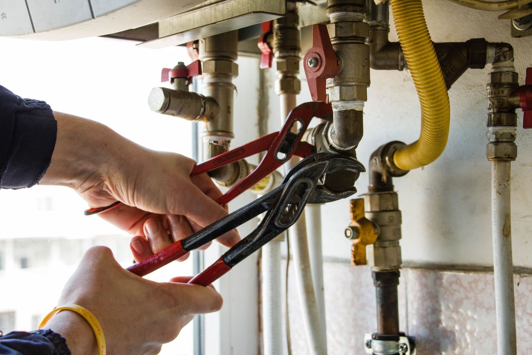 A person is fixing a water heater with a wrench.