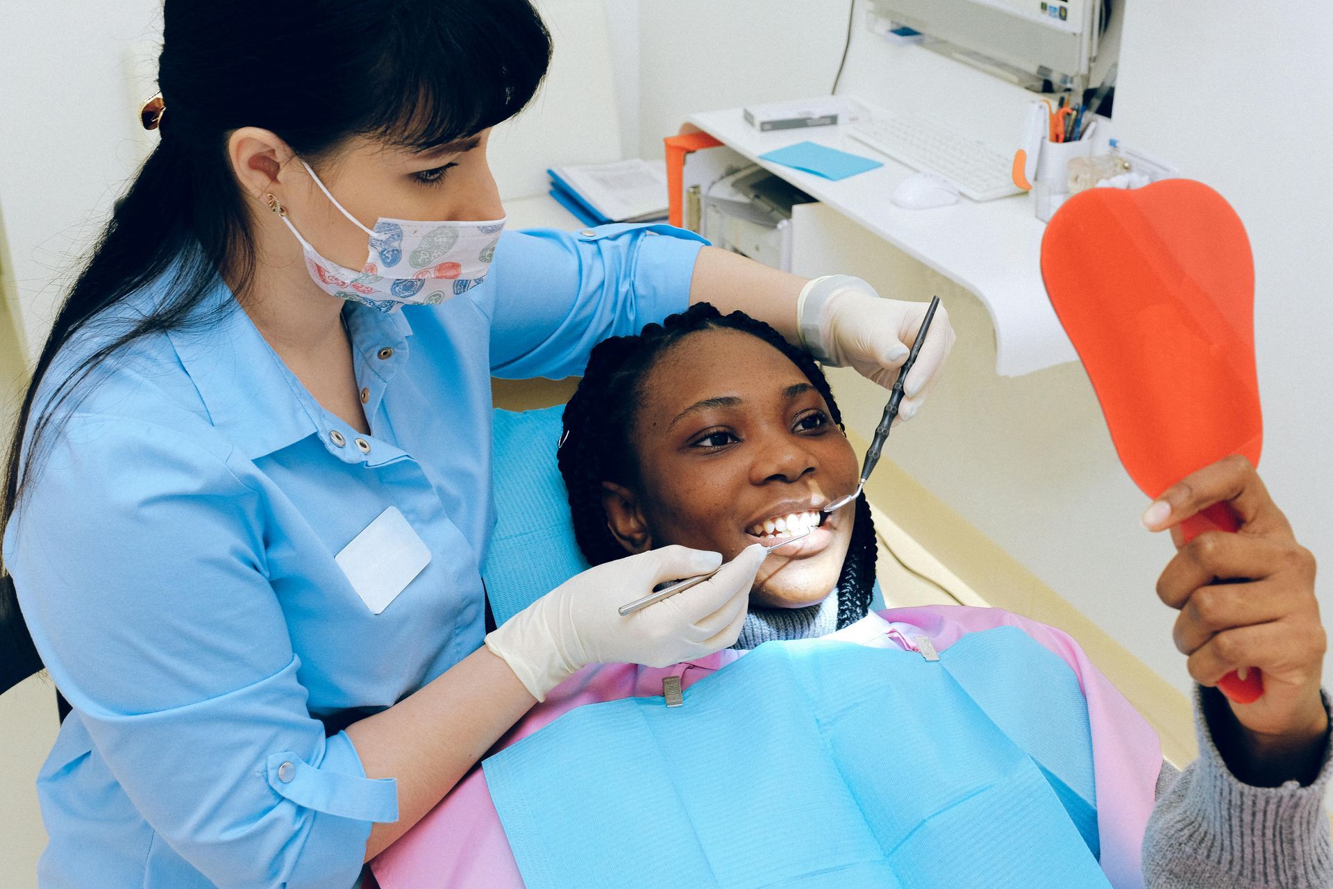 A woman is sitting in a dental chair while a dentist examines her teeth.