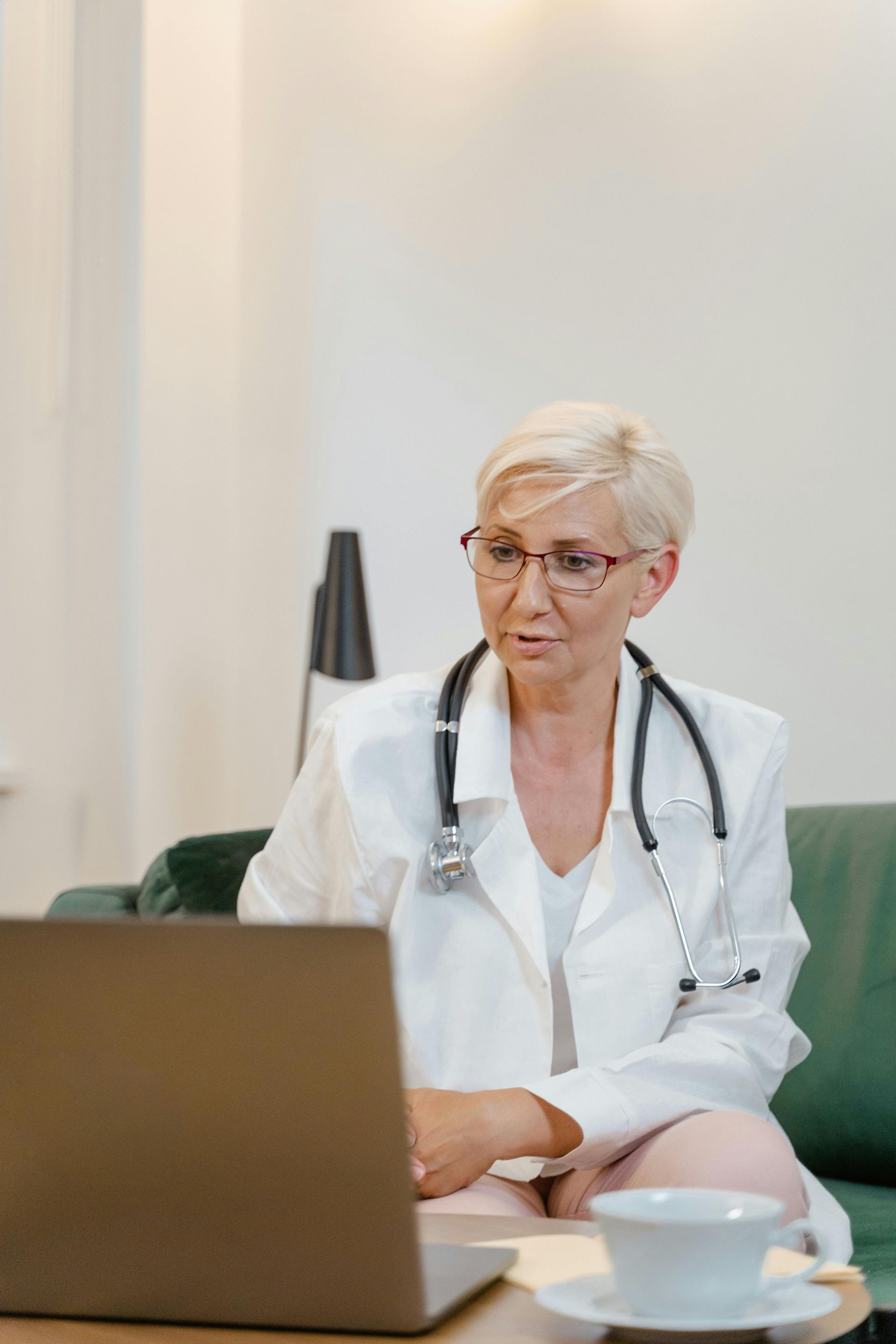 A female doctor is sitting at a table using a laptop computer.