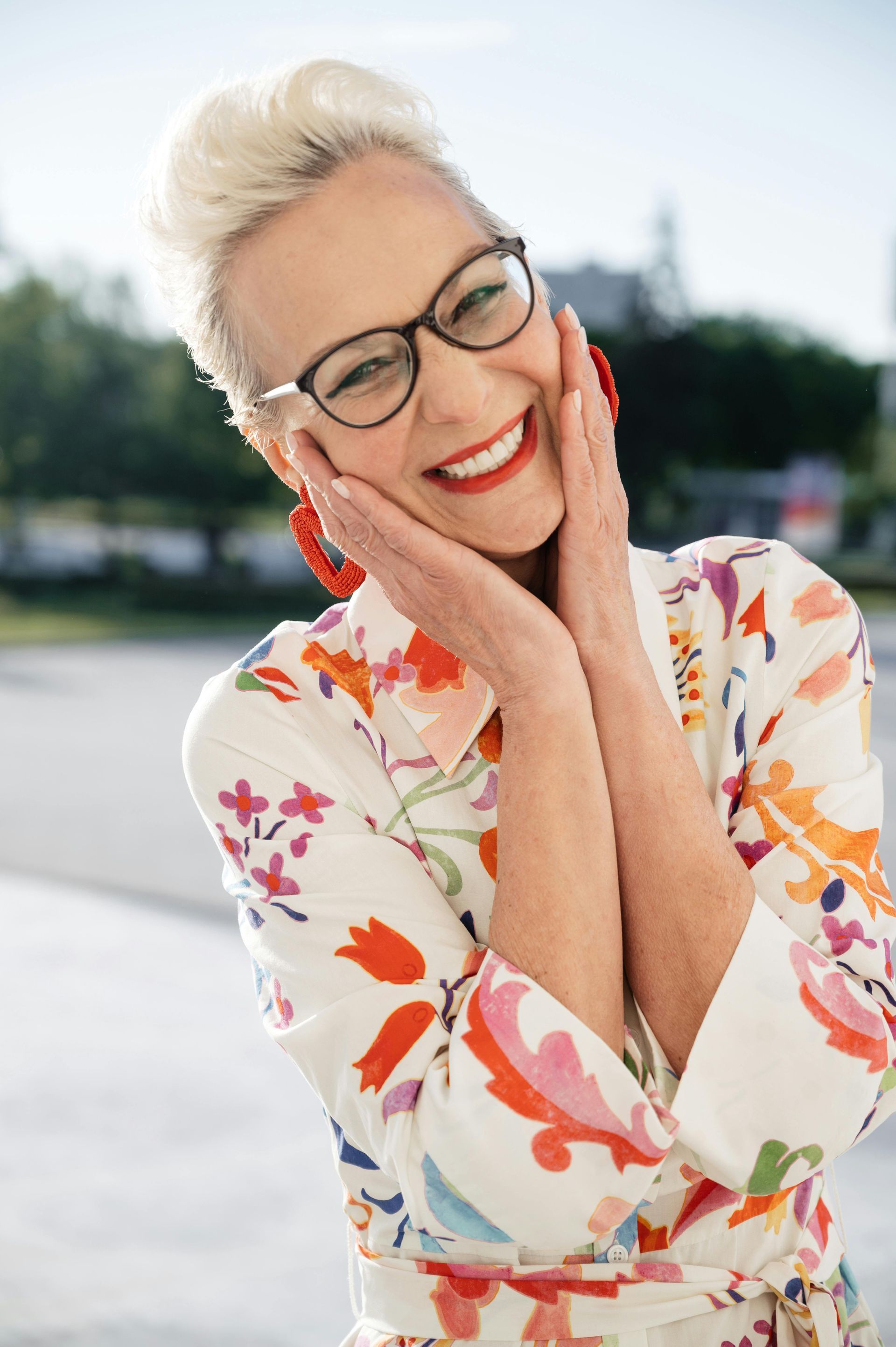 A woman wearing glasses and a floral dress is smiling.