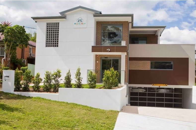 A modern two-story building with white walls, brown accents, and an underground garage, fronted by a manicured lawn.