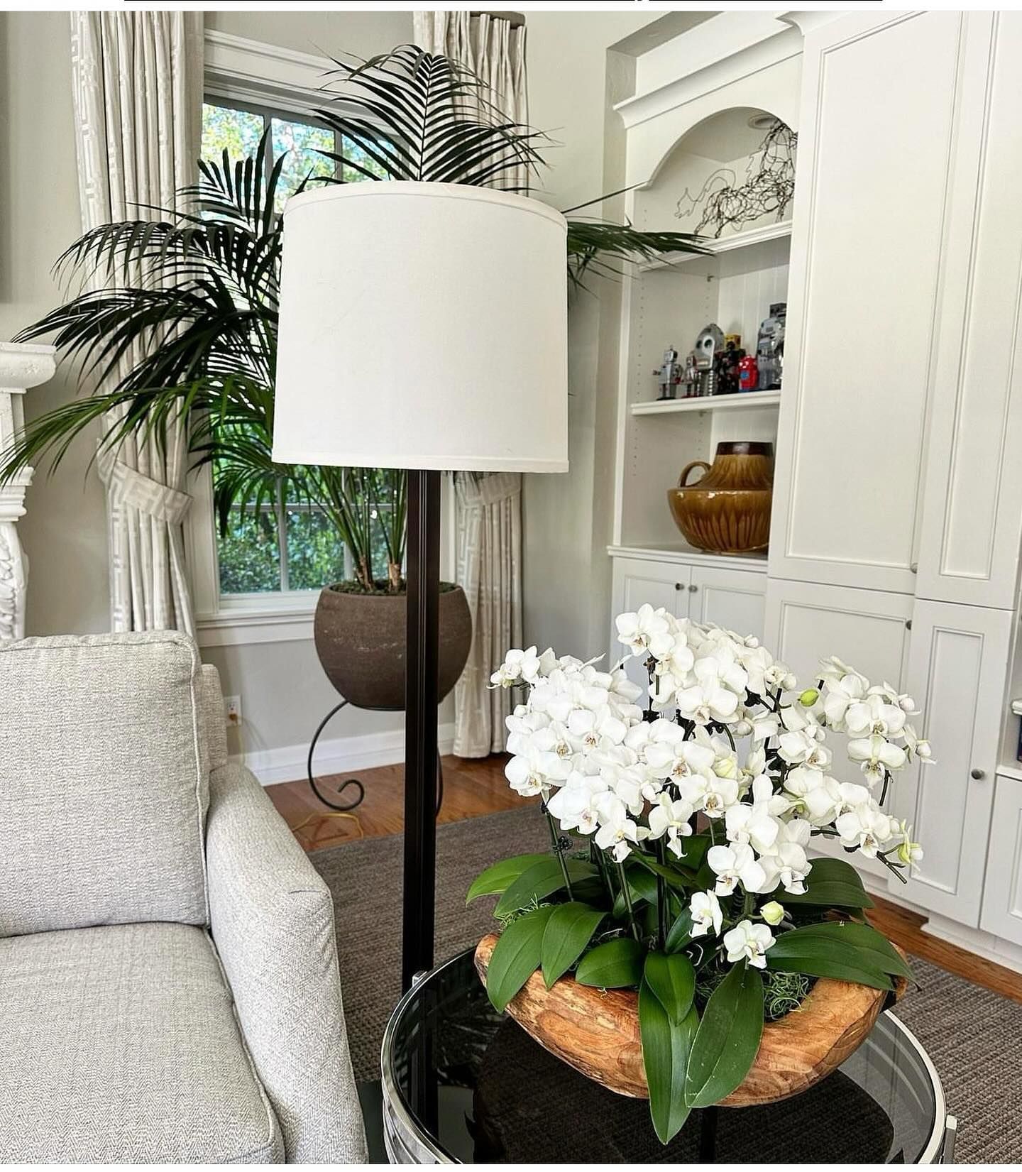 Living room with a tall white lamp, an armchair, white orchids, and a built-in white cabinet.