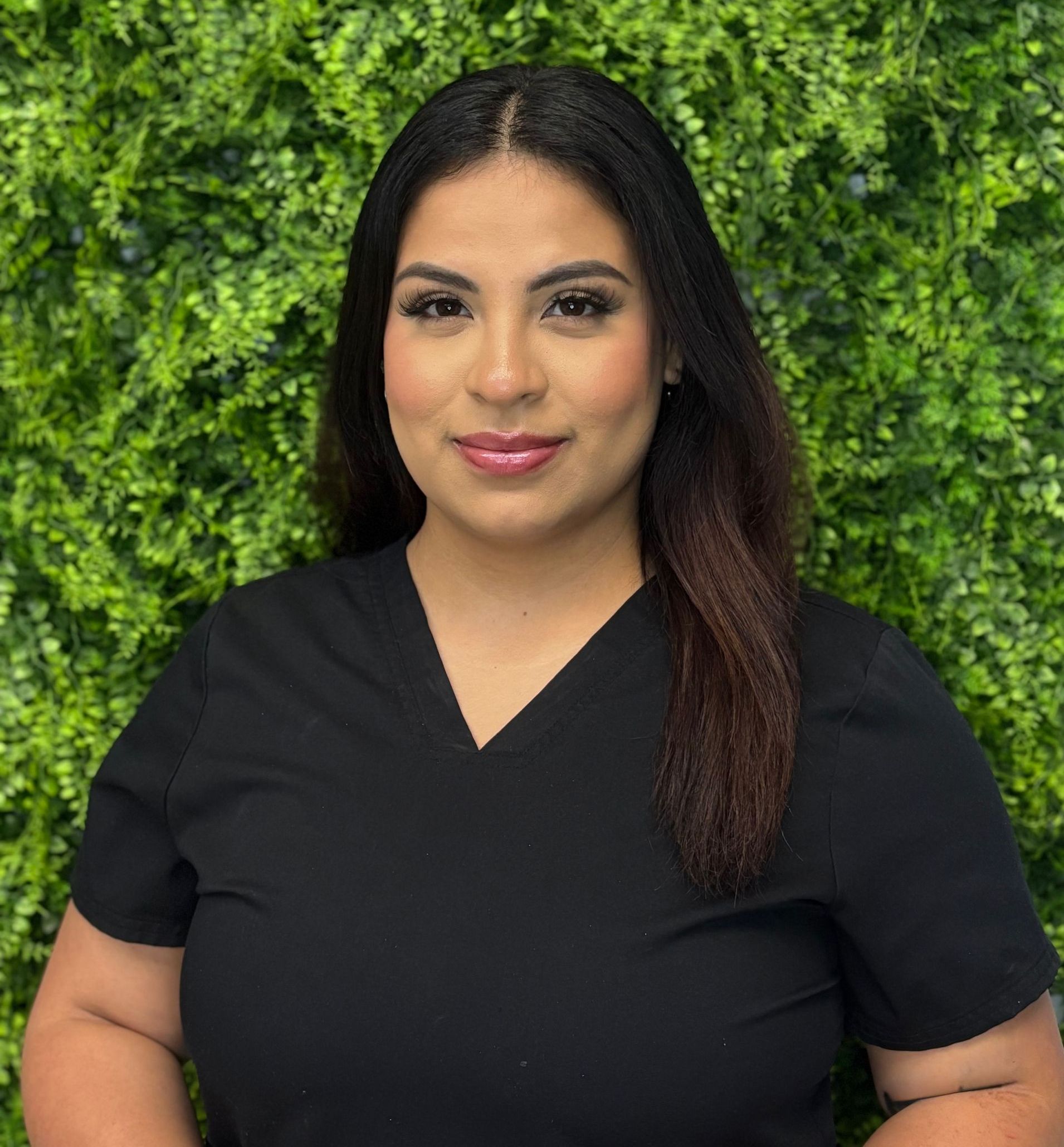 A woman in a grey scrub top is smiling in front of a green wall.