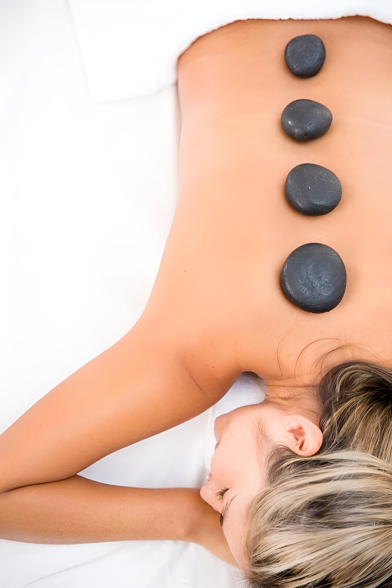 A Woman is Laying on a Bed With Four Black Rocks on Her Back — Nonny Thai Healing Massage In Coffs Harbour, NSW