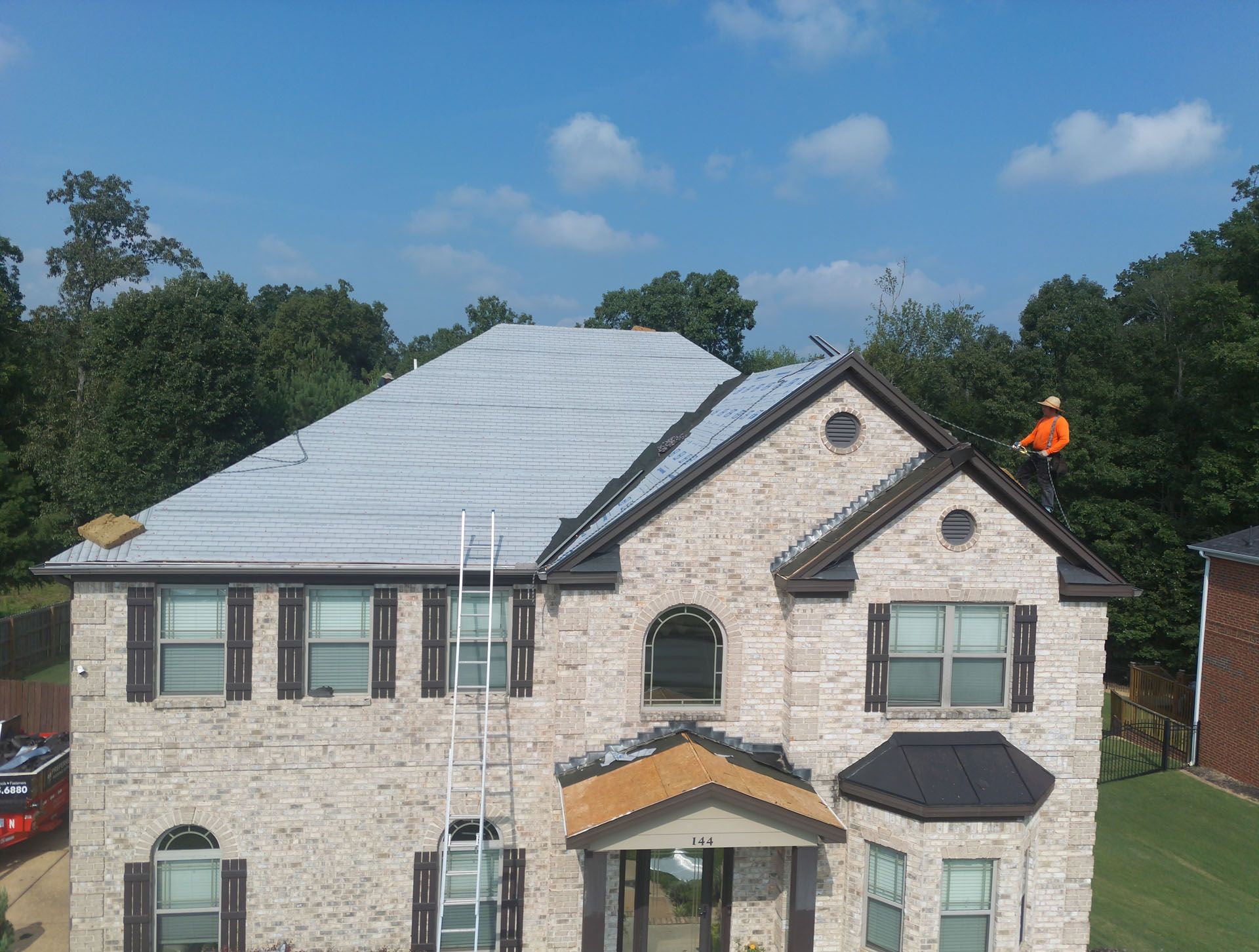 A man is working on the roof of a large brick house.