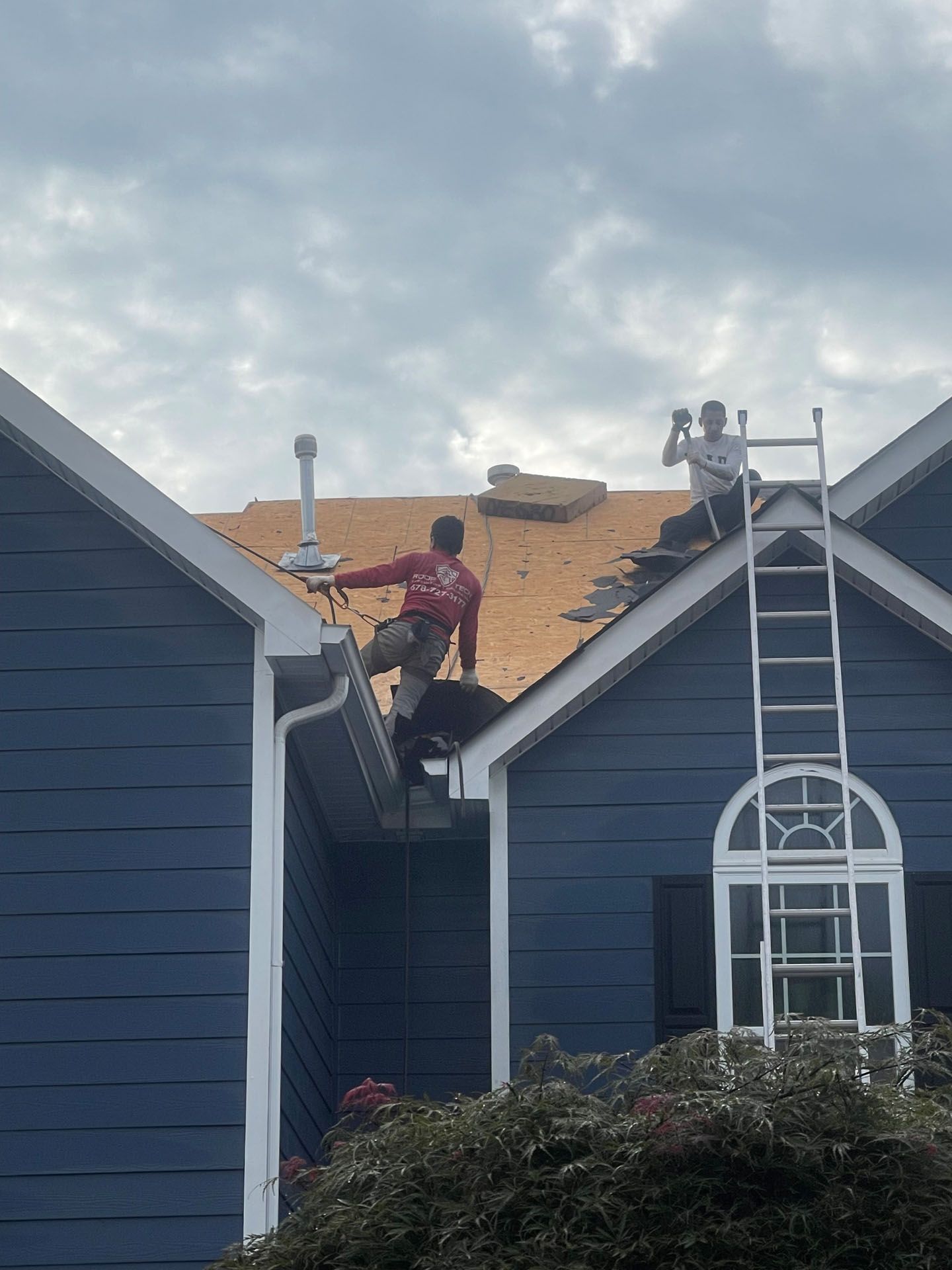 Two men are working on the roof of a blue house.