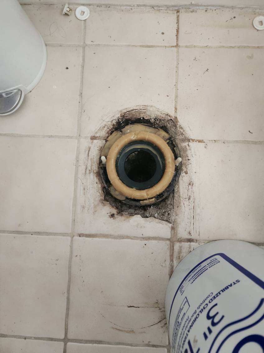 A hole in the floor of a bathroom next to a toilet.