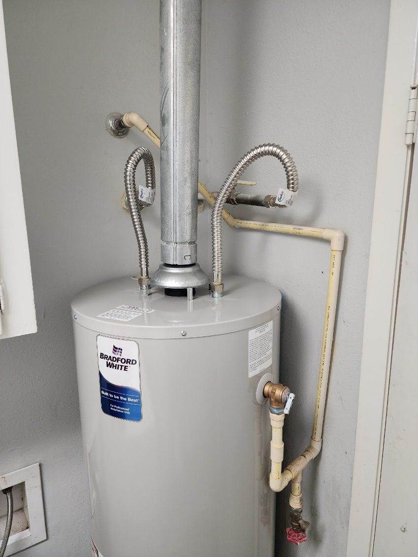 A water heater is sitting in a corner of a room next to a door.