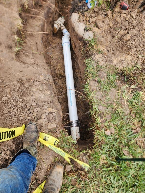 A person is laying in the dirt next to a pipe in the ground.