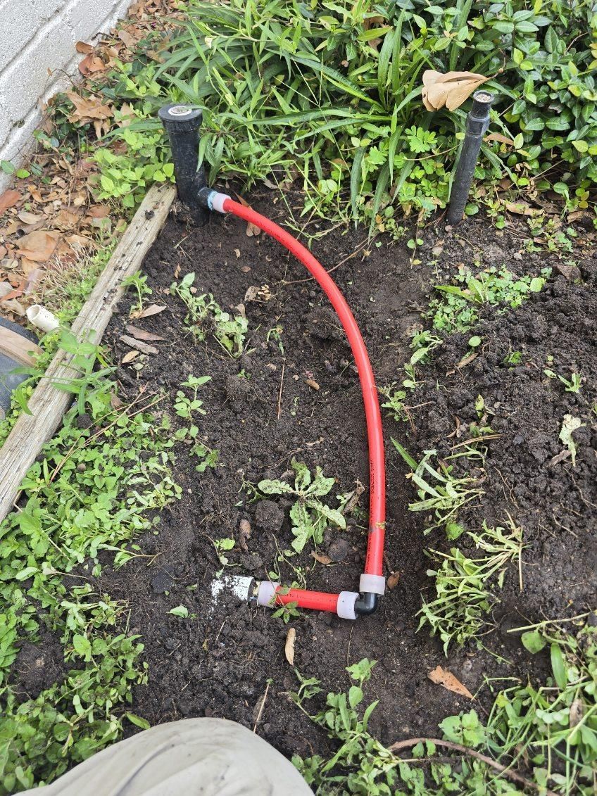 A red hose is laying in the dirt next to a sprinkler.