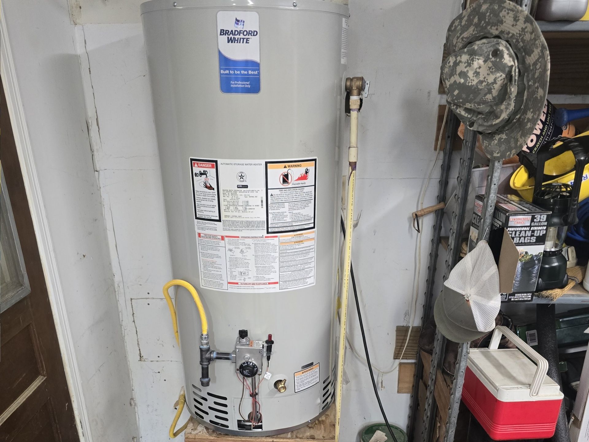 A gas water heater is sitting on a wooden shelf in a garage.