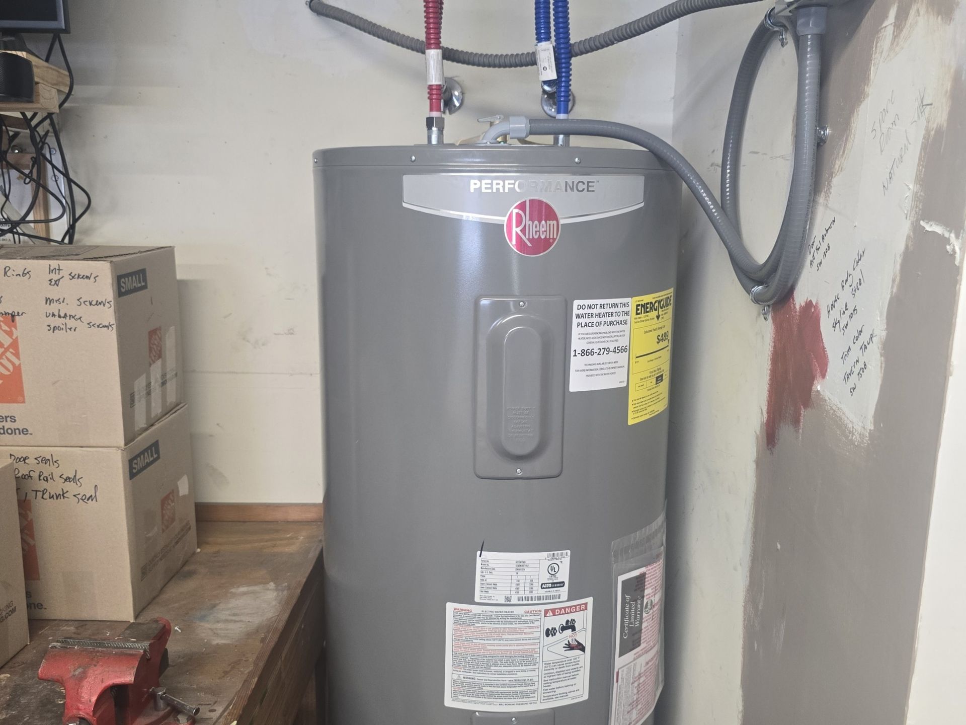 A gray water heater is sitting in a room next to a wall.