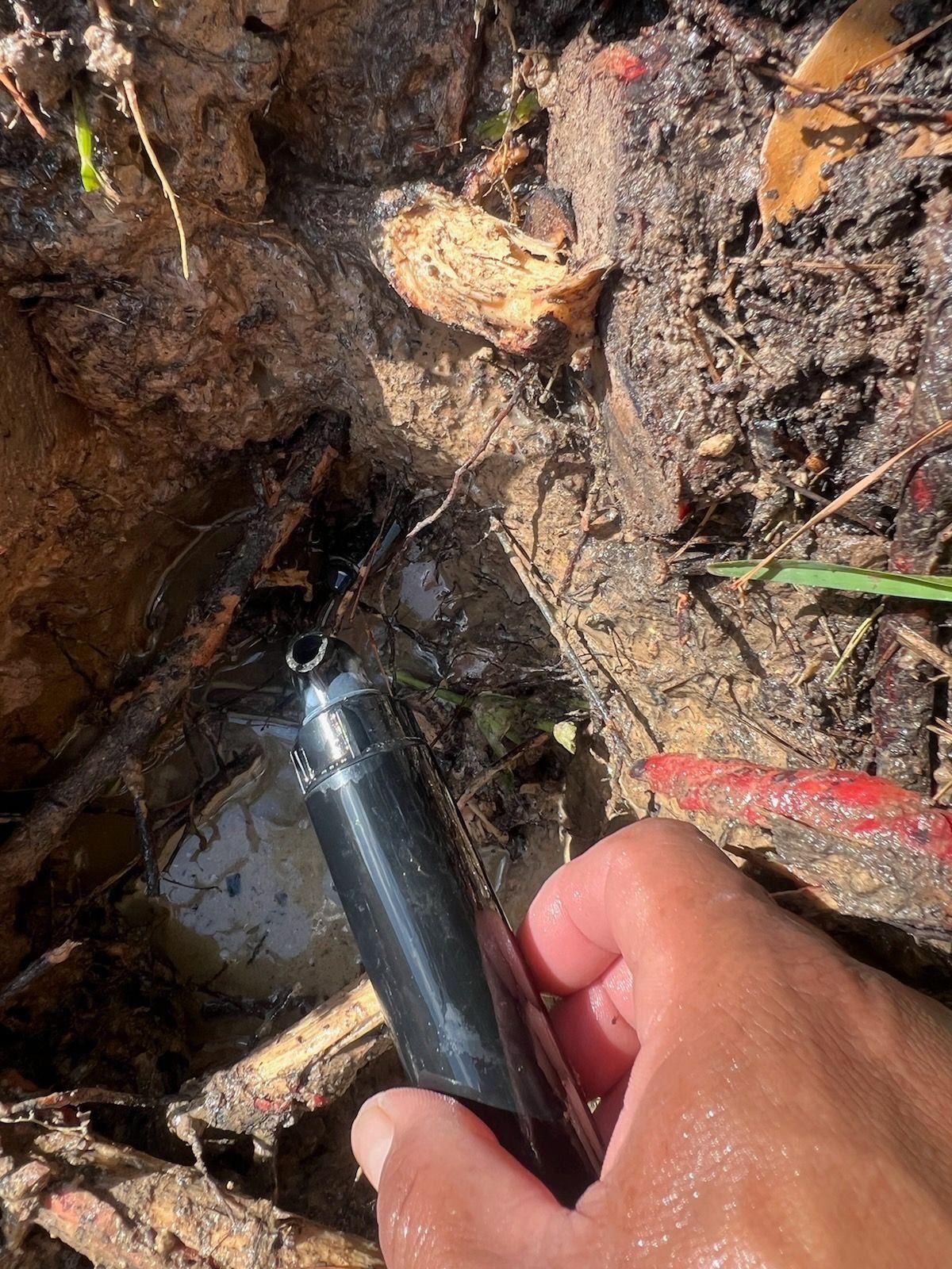 A person is holding a black pipe in their hand in the dirt.