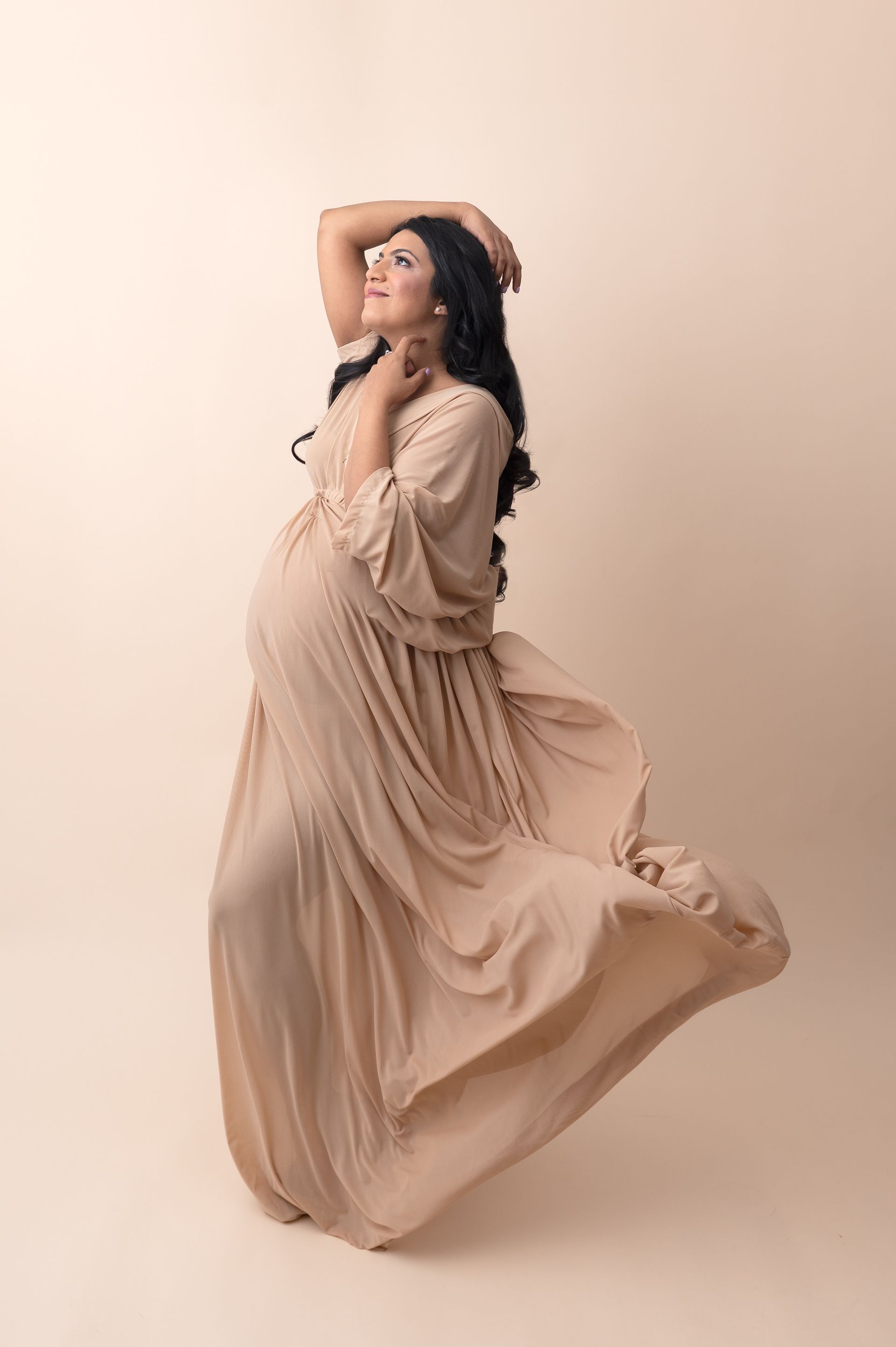 a pregnant woman in a long dress is standing on a beige background .