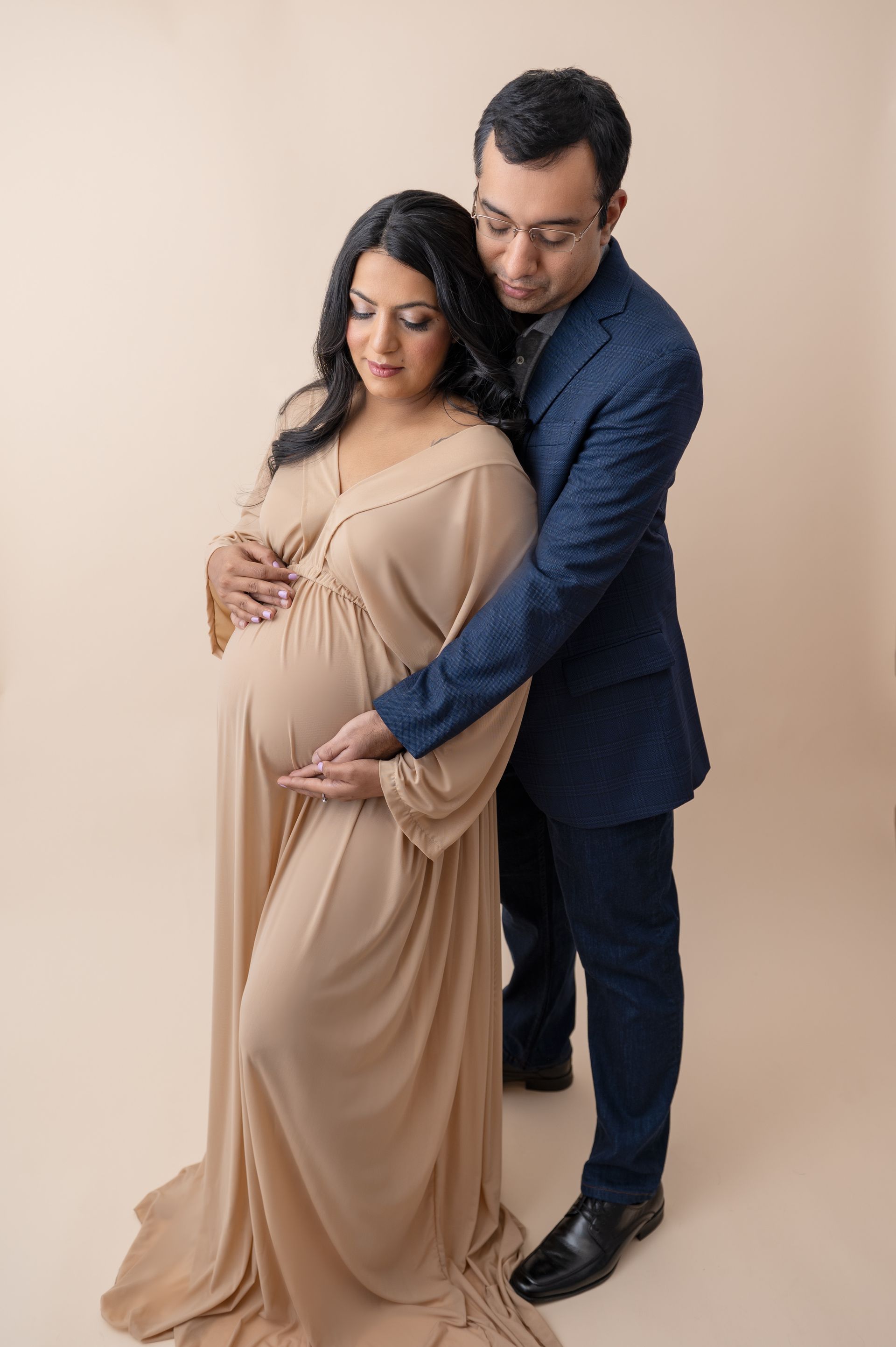 a man in a suit is hugging a pregnant woman in a dress .