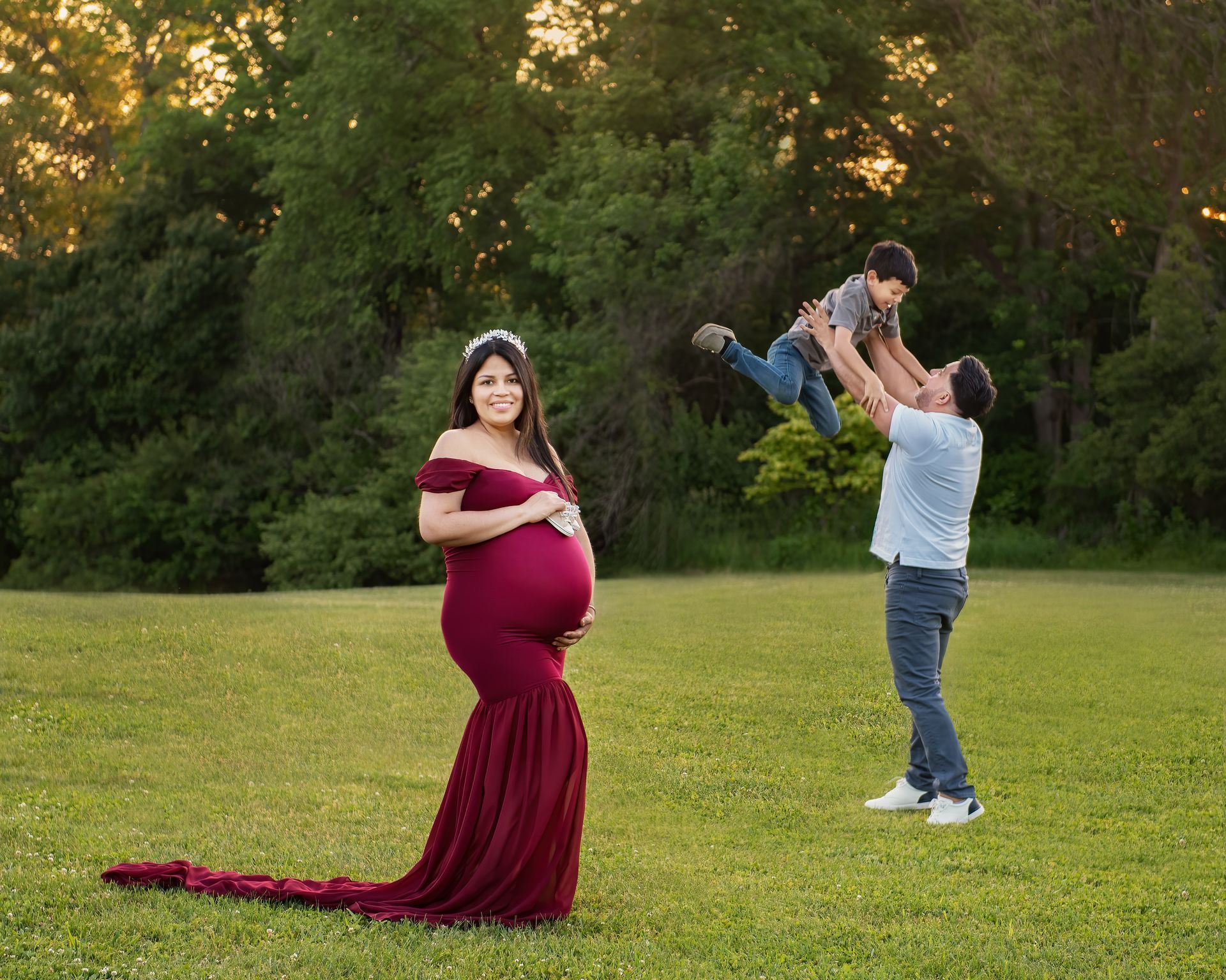 a pregnant woman is standing in a field with her husband and son .