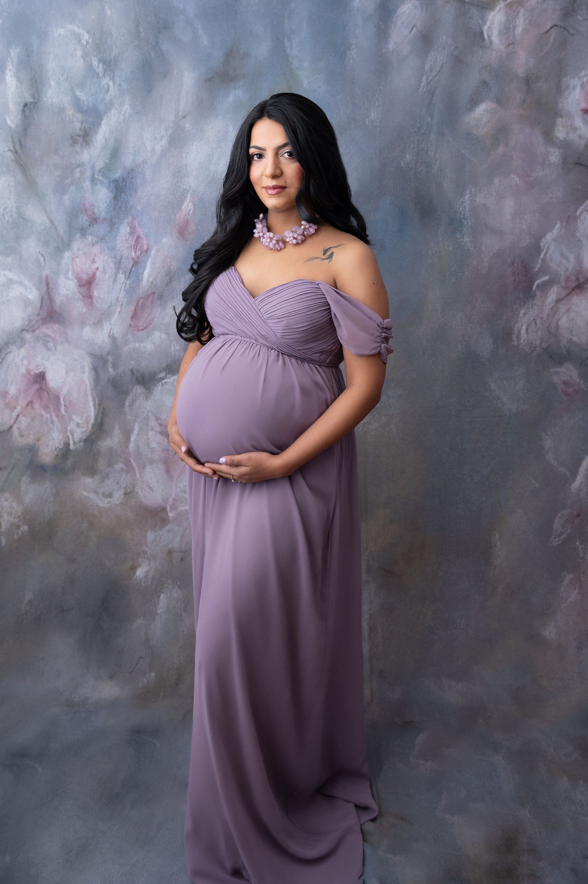 a pregnant woman in a purple dress is standing in front of a floral background .