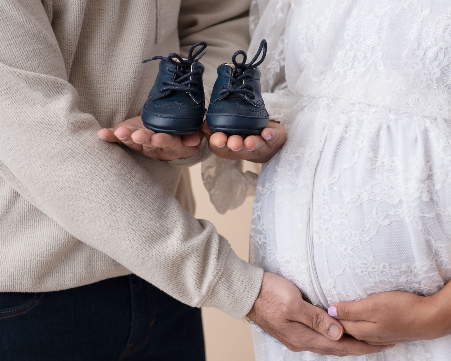 a pregnant woman is holding a pair of baby shoes in her hands .