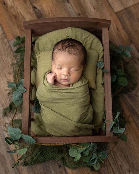 a newborn baby wrapped in a green blanket is sleeping in a wooden crib 
