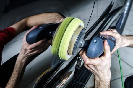 Two people buffing a car's chrome trim with electric polishers.