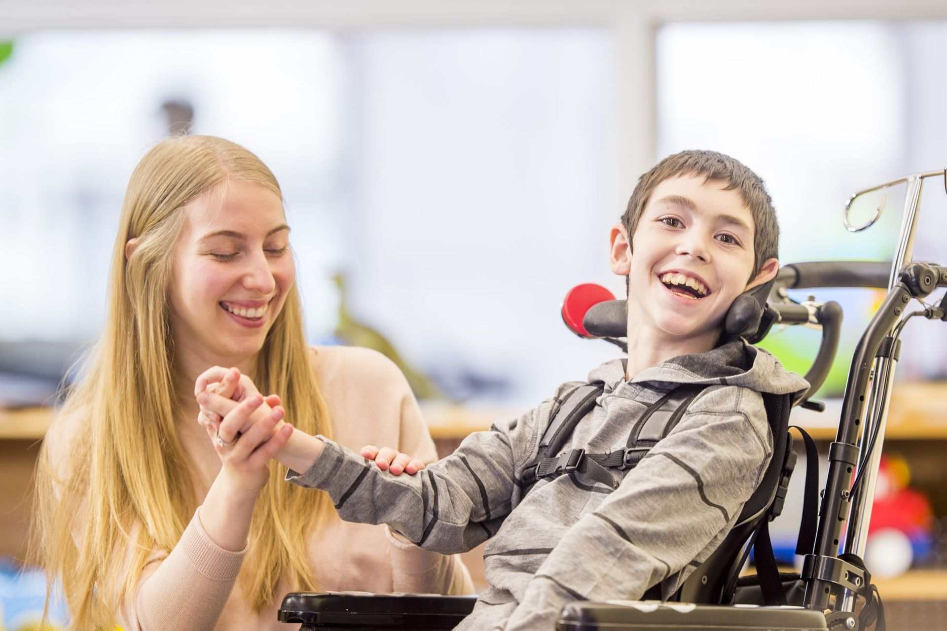 Young blonde lady smiling while holding the hand of a young,smiling boy with cerebral palsy. 