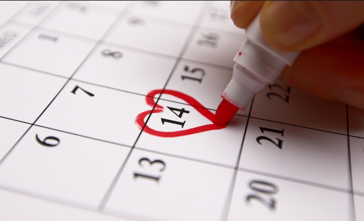 The tip of a marker is drawing a heart shape around a particular date on a calendar